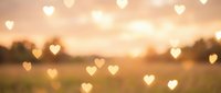 Romantic heart-shaped bokeh lights overlay on blurred sunset landscape background for Valentine's Day cards, wedding invitations and love themes.