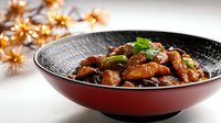 Braised chicken with mushrooms in Asian style sauce garnished with fresh herbs, served in black and red bowl against festive golden lights background.