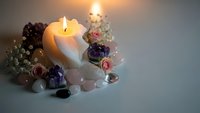 Burning candle surrounded by healing crystals, gemstones and dried flowers creating peaceful spa atmosphere for meditation and wellness rituals.