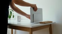 Person with medium skin tone operating a modern air purifier on a wooden desk with potted plant and cup, demonstrating home air quality improvement and indoor wellness technology.