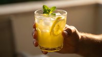 Refreshing golden beverage with ice and fresh mint leaf held in hand, perfect for summer drinks, cocktails, mocktails, and beverage advertising campaigns.