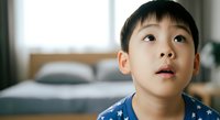 Young Asian boy in blue star-patterned shirt looking upward with wonder and curiosity indoors. Suitable for parenting, childhood development, education, and family lifestyle content.