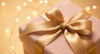 Pink gift box with golden ribbon bow and fairy lights creating warm festive atmosphere for holidays and special occasions.
