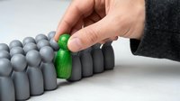 Hand selecting one green figure from a group of gray figures, representing uniqueness, leadership, standing out from crowd, individuality, and business differentiation concept.