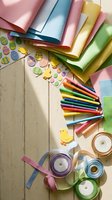 Colorful craft supplies arranged on wooden surface with paper sheets, colored pencils, ribbons and decorative stickers for creative projects and scrapbooking.