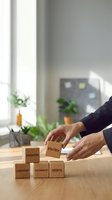 Close-up of hands arranging wooden blocks with business strategy words on modern office desk near window with plants, representing corporate planning and development.