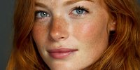 Young redhead woman with freckles and blue eyes looking at camera with natural makeup and wavy hair for beauty and skincare concepts.