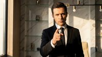 Confident businessman in black suit pointing finger at camera in modern office with marble wall and warm lighting for corporate presentations.