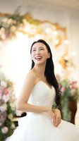 Happy Asian bride in white wedding dress smiling joyfully at elegant ceremony venue with floral decorations and warm lighting for wedding photography.