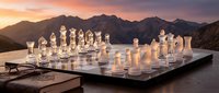 Glass chess set on wooden table with dramatic mountain sunset backdrop creating elegant strategic game atmosphere for luxury lifestyle concepts.