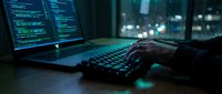 Programmer coding at night with laptop displaying code on screen, hands typing on keyboard in dark office environment with city lights background.