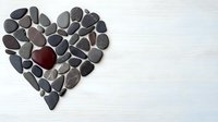Heart shape arranged from gray beach stones with single red stone in center on white wooden background. Minimalist romantic composition with copy space.