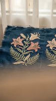 Vintage blue denim fabric with delicate pink and green floral embroidery featuring lily motifs and fern leaves on frayed textile near window.