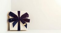 Cream-colored gift box with dark navy ribbon bow on neutral background, isolated for holiday, celebration, and packaging design projects.