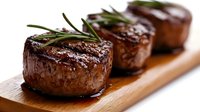 Grilled beef steaks with rosemary herbs on wooden cutting board. Juicy meat medallions with grill marks and fresh garnish for restaurant menu and cooking.