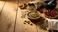 Aromatic spices and herbs scattered on rustic wooden table with burlap sack, mortar and pestle. Culinary ingredients for cooking and seasoning dishes.