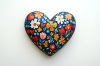 Colorful floral heart-shaped painted stone with folk art style flowers in red, yellow, white, and orange on dark blue background against white surface.