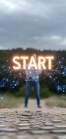 Glowing orange START text with network connections floating above blurred person standing on path, dramatic cloudy sky background. For motivation and business concepts.