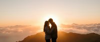 Romantic couple silhouette embracing at mountain summit during golden hour sunrise with dramatic clouds and warm light for love and relationship concepts.