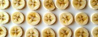 Fresh sliced banana rounds arranged in neat rows showing star-shaped centers on white background, overhead view pattern for healthy food and fruit design.