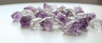 Raw amethyst and clear quartz crystal chunks scattered on white surface for mineral collection, healing, jewelry design, and spiritual wellness projects.