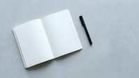 Open blank notebook with black pen on gray concrete surface, ready for writing, planning, or design mockups.