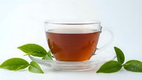 Glass cup of aromatic black tea with fresh green leaves on white background. Hot beverage for relaxation and wellness concepts.