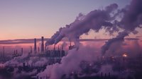 Industrial factory chimneys emitting smoke at sunset creating atmospheric purple and pink sky with dramatic silhouettes of manufacturing plant and pollution.