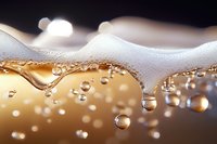 Golden liquid with white foam and rising bubbles in macro photography, showing carbonation and refreshing beverage details against dark background.