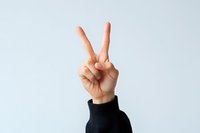 Caucasian hand showing peace sign or victory gesture against white background, wearing black sleeve. Positive nonverbal communication concept.