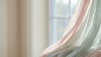 Soft flowing curtains in pastel pink and sage green tones create dreamy window treatment with natural light filtering through delicate fabric layers.