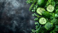 Fresh green vegetables and herbs arranged on dark stone background with copy space for healthy eating and cooking concepts.