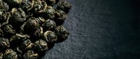Dried hops pellets scattered on dark slate surface, used for brewing craft beer and adding flavor, aroma, and bitterness to beverages.