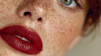 Close-up portrait of young Caucasian woman with freckled skin and bold red lipstick. Natural beauty concept for cosmetics and skincare campaigns.