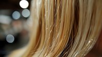 Macro shot of blonde hair strands with water droplets and bokeh lights in background creating dreamy atmosphere for beauty and haircare advertising.
