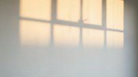 Sunlight streaming through window panes casts geometric shadows on white wall, creating warm light patterns ideal for backgrounds and interior design projects.