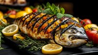 Grilled whole fish with herbs and lemon slices on dark slate, garnished with fresh mint and rosemary. Gourmet seafood dish for restaurant menus and cooking.
