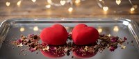 Pair of red velvet heart-shaped desserts on dark plate with crumbled chocolate garnish and bokeh lights, romantic Valentine's Day or wedding celebration food styling.