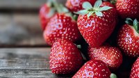 Fresh ripe strawberries with green leaves on rustic wooden background, macro shot showing detailed texture and natural juicy appearance. Food photography.