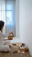 Woman in white clothing practicing meditation with singing bowl and crystals in bright minimalist room for wellness and mindfulness rituals.