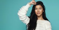 Young Asian woman with long black hair wearing white sweater posing confidently against turquoise background for lifestyle and fashion content.