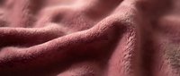 Soft coral pink fleece fabric with gentle folds and texture, cozy material for blankets, clothing and home decor projects.