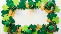 Festive St. Patrick's Day frame with green shamrocks, leprechaun hats, horseshoes and gold coins on white background for holiday greeting cards and decorations.