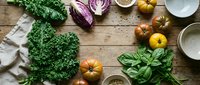 Fresh organic vegetables and herbs arranged on rustic wooden table with empty bowls ready for healthy cooking and meal preparation.