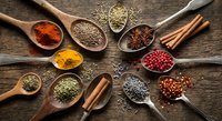 Aromatic spices and herbs in wooden spoons arranged on rustic wood background for culinary cooking and seasoning recipes.