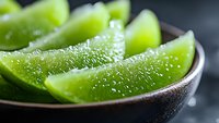Fresh lime wedges with water droplets in black ceramic bowl, macro shot showing juicy citrus fruit texture and vibrant green color. Perfect for cocktail and food photography.