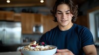 Young Hispanic man enjoying healthy breakfast bowl with oatmeal berries and nuts in modern kitchen smiling happily at nutritious morning meal.