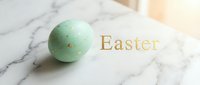 Mint green Easter egg with gold speckles on a marble surface beside elegant gold Easter text, soft warm light.