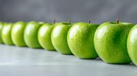 Fresh green apples arranged in diagonal line on light gray background, selective focus with water drops on glossy surface. Concept of healthy eating and freshness.