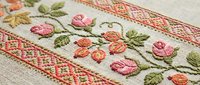 Traditional floral embroidery on linen fabric with pink and coral roses, green leaves in cross-stitch pattern. Handcrafted textile art for home decor projects.